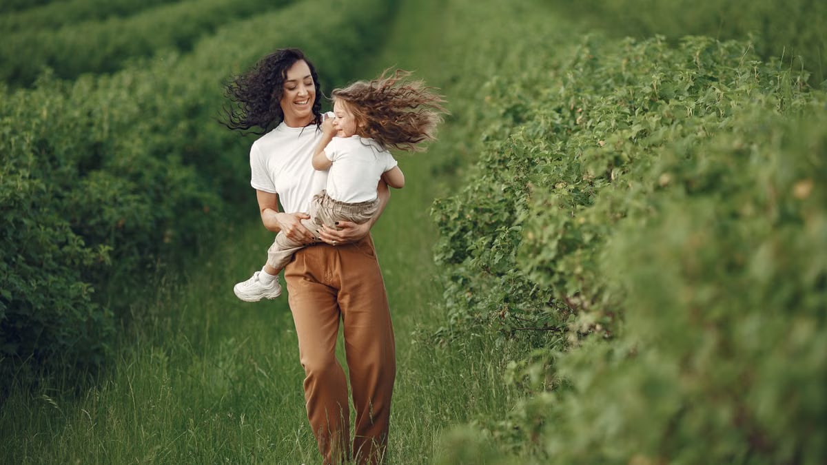 A happy mother and daughter run together through a lush green field in summer, celebrating family and nature.